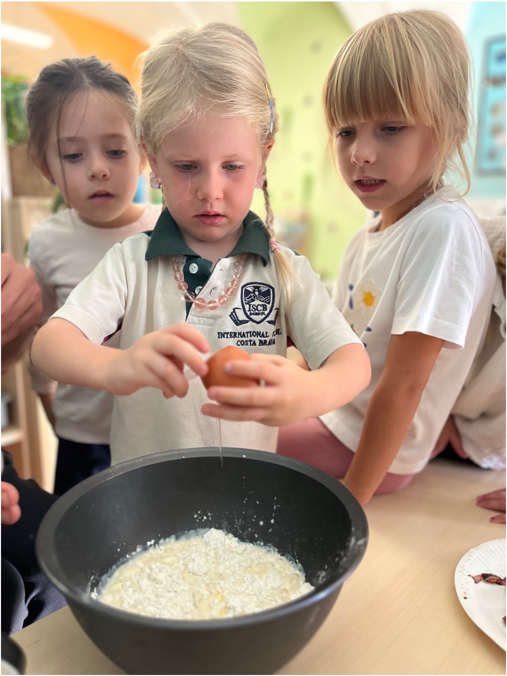 An ISCB Early Years pupil cracking an egg into a bowl with classmates